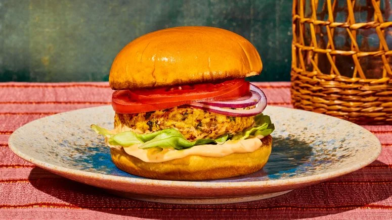 chicken burger on a colorful plate on pink surface with a blue backdrop and basket in the background