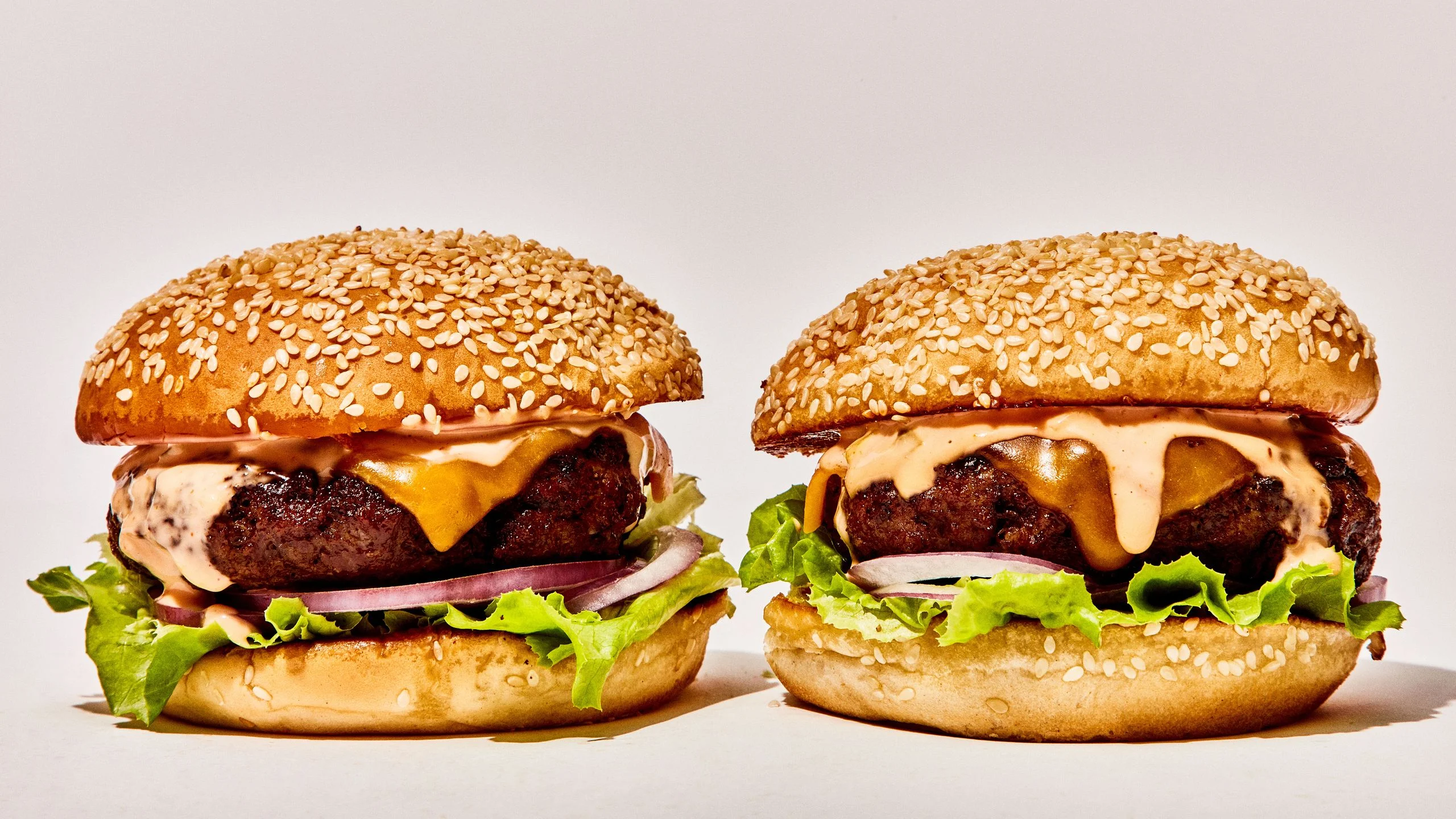 Two cheeseburgers on seeded buns with lettuce red onion and secret sauce.