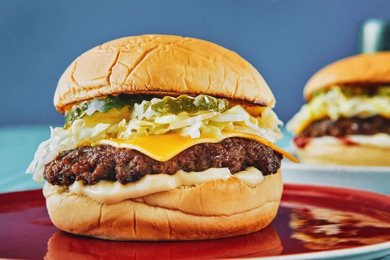 A smash burger beef patty on a toasted potato bun with mayonnaise shredded iceberg lettuce a slice of American cheese...