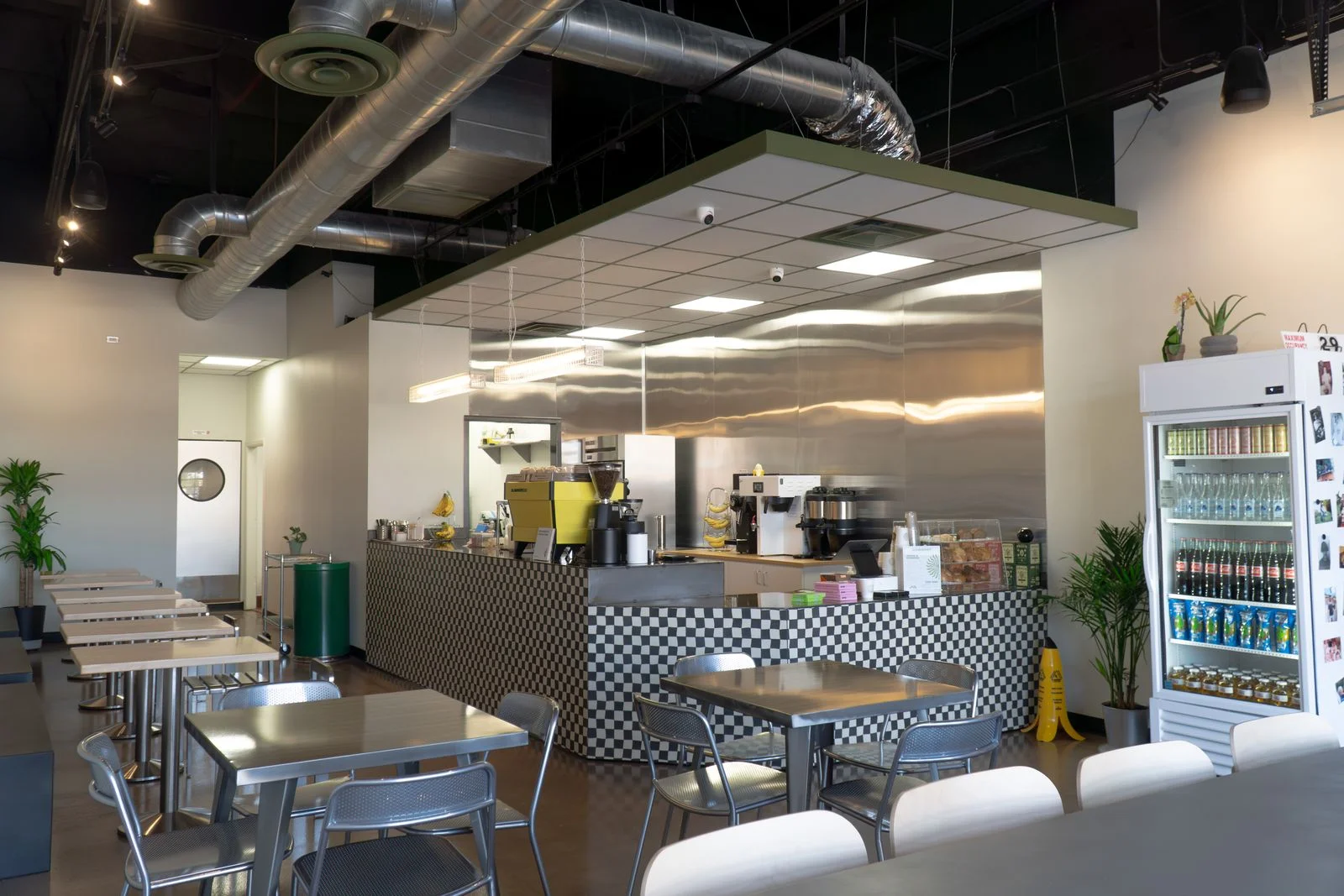 A wide view of a restaurant interior comprised of metal furniture and blackandwhite checkered wallpaper at the food counter.