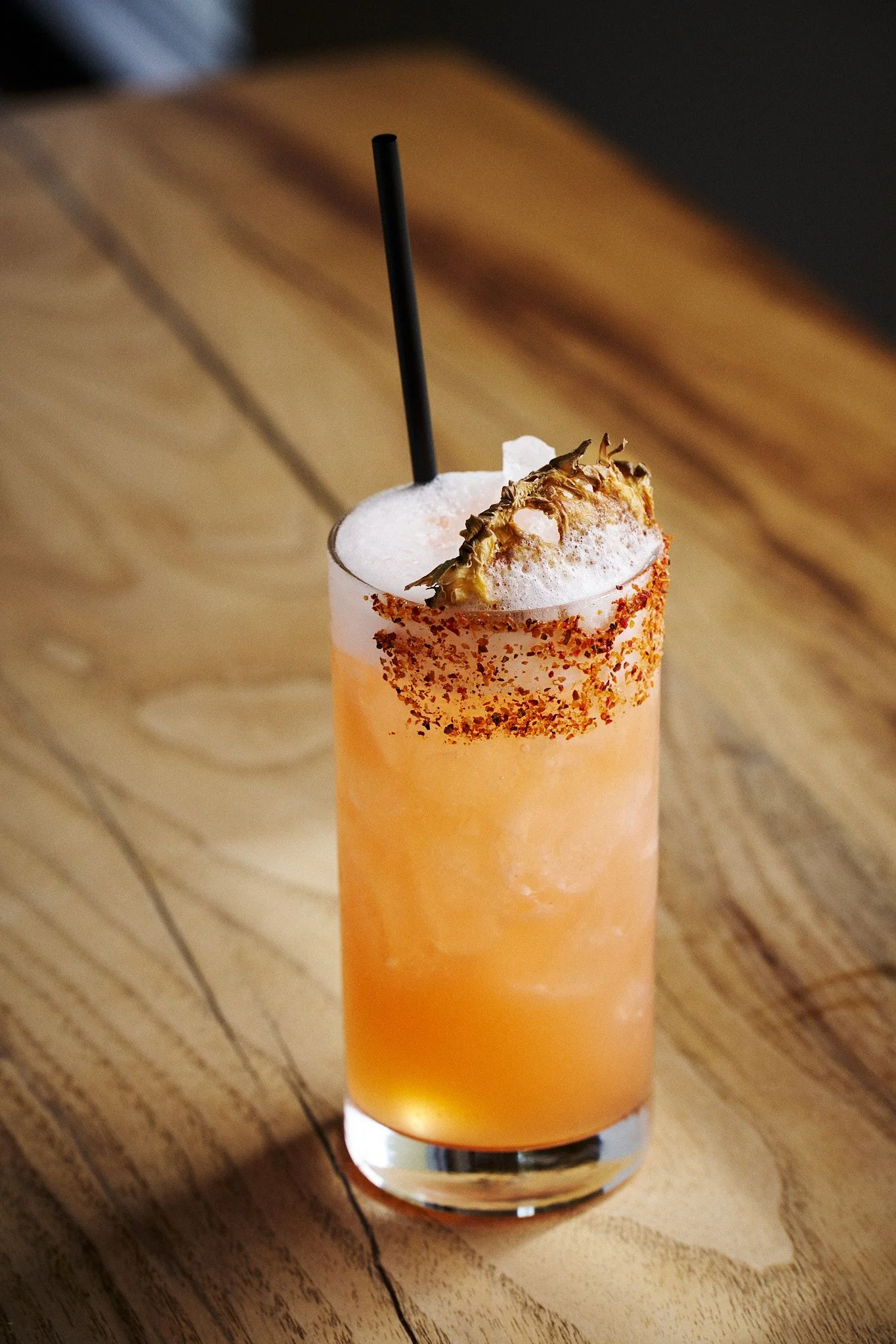 A creamsicklecolored cocktail with a seasoned rim on a wood table.