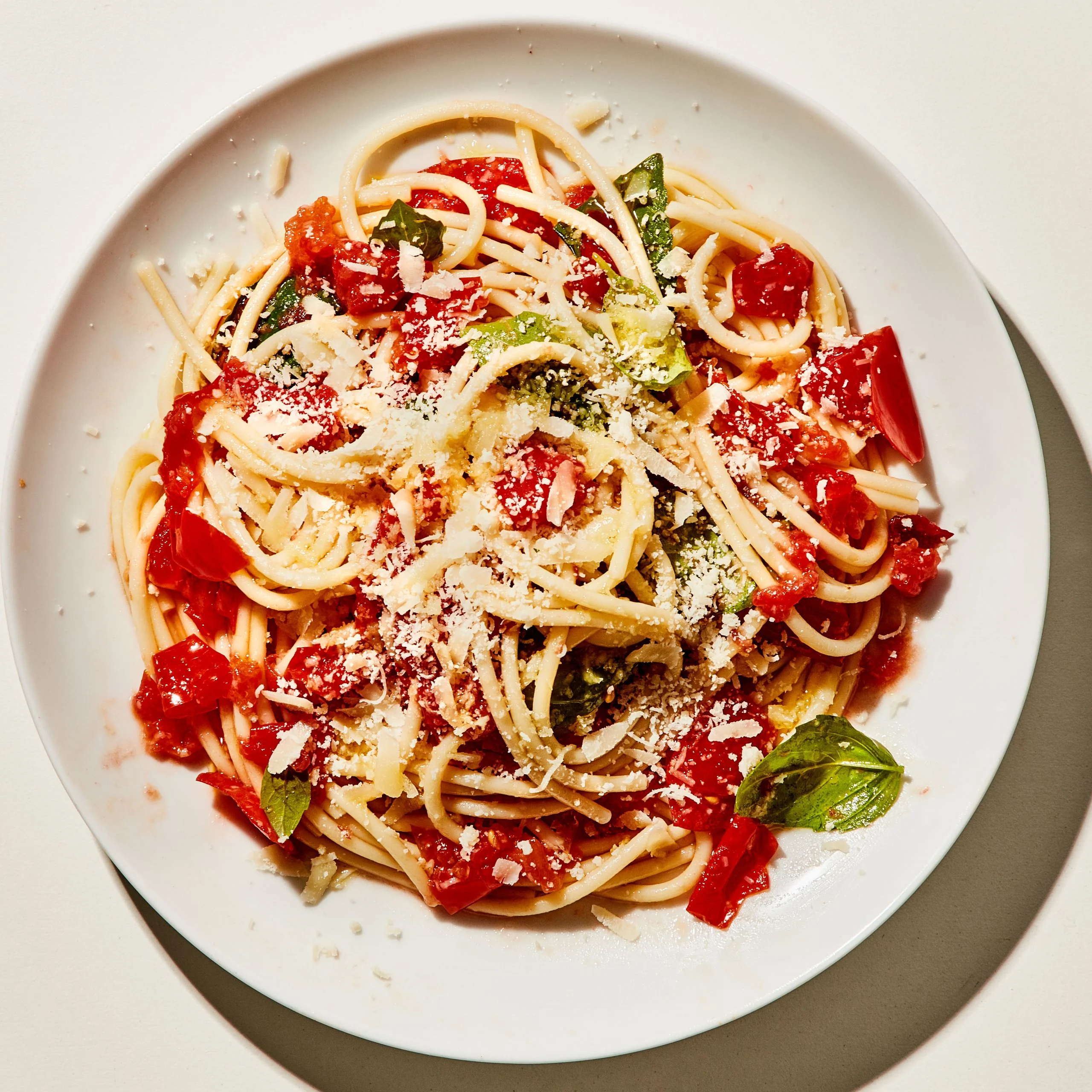 A plate of fresh tomato pasta with buccatini bright red splotches of smashed tomato and torn basil leaves.