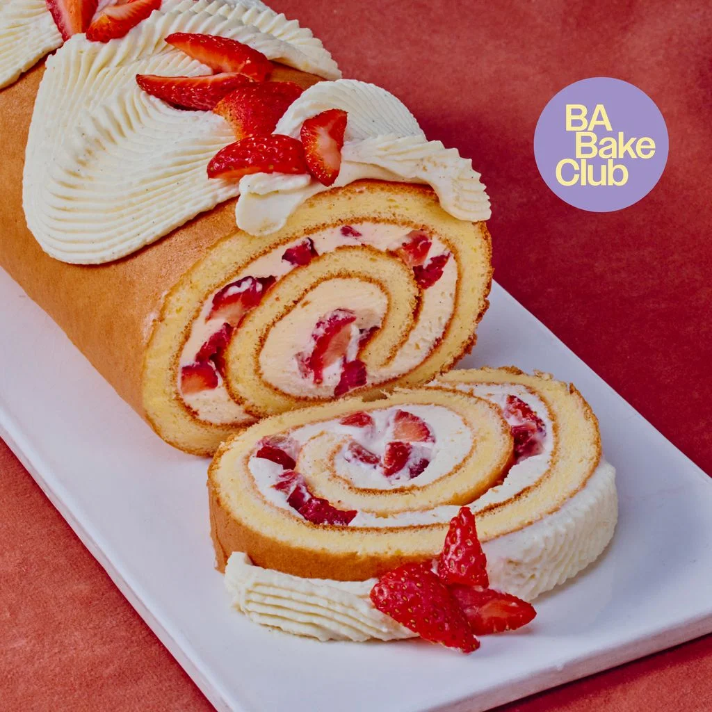 A cutinto strawberry swiss roll on a white platter all atop a red suede background.