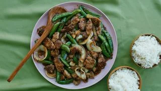 Ginger glazed pork snap peas garlic and onions on a serving platter with bowls of white rice.