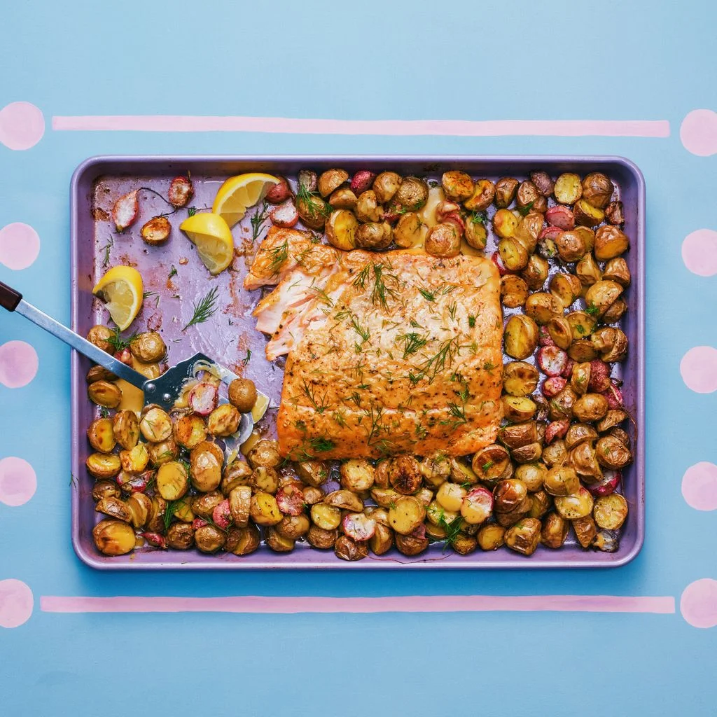 A sheet tray filled with potatoes on a blue and pink background with