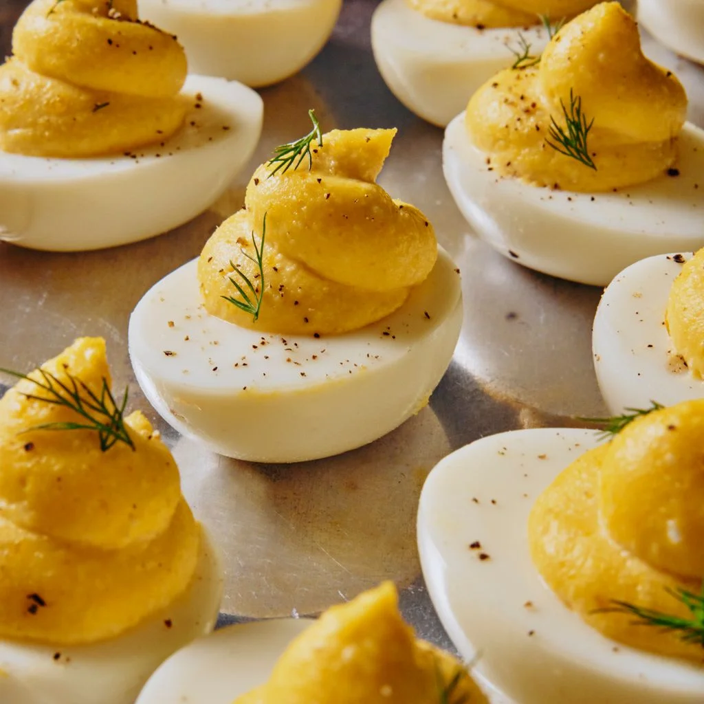 A multitude of deviled eggs garnished generously with pepper and dill sprigs on a reflective silver platter.