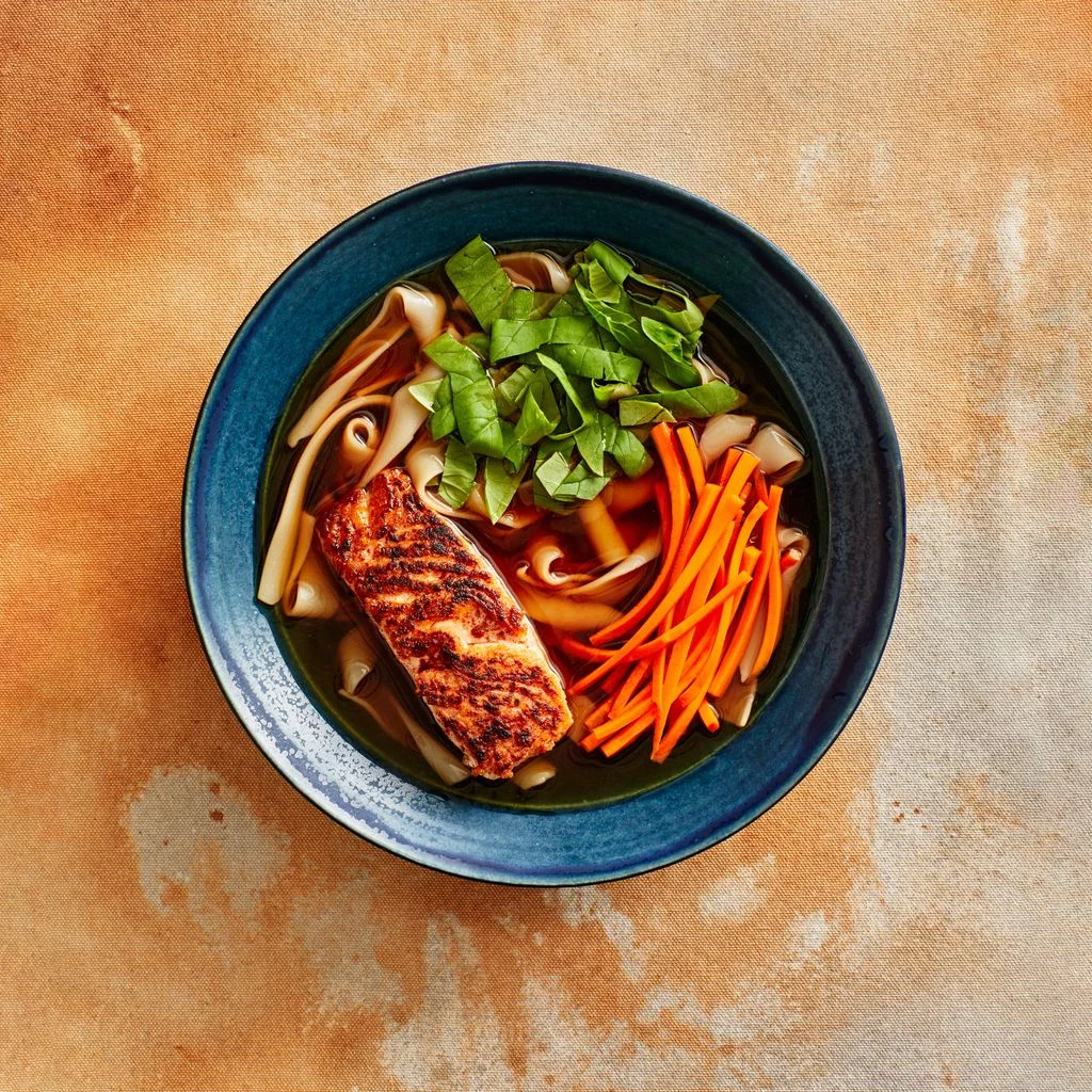 Spiced Salmon Noodle Soup in a dark blue plate on a a rusted colored background
