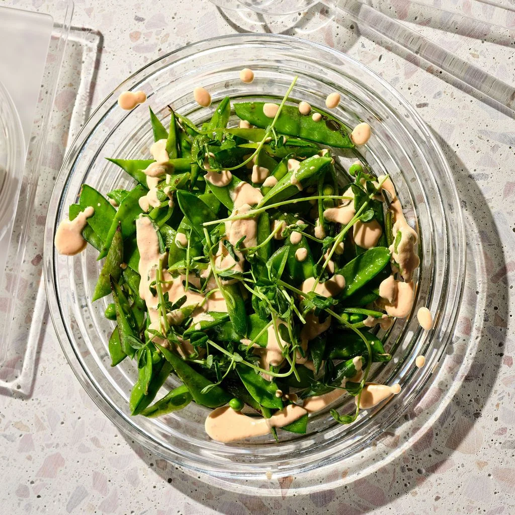 An assortment of snow peas and snap peas in a bowl drizzled with a creamy sauce.