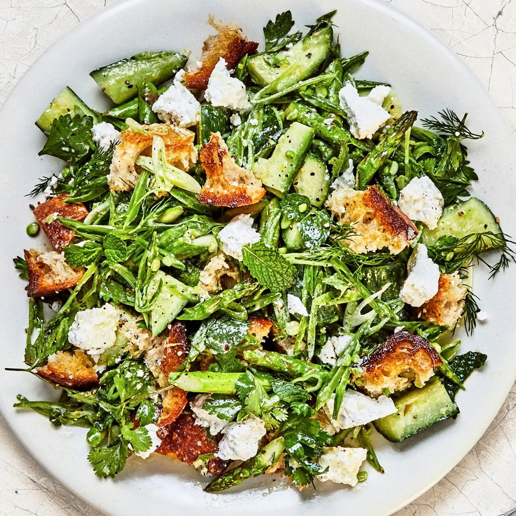 Spring panzanella salad with smashed cucumbers blistered asparagus and lots of herbs on a platter.