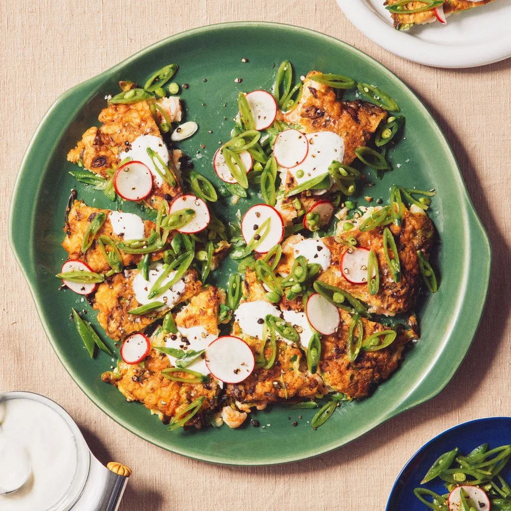 Shrimpstudded eggy pancakes topped with snap peas sliced radishes sour cream and black pepper.