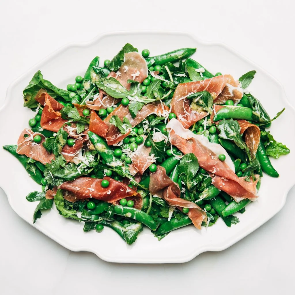 A serving platter of peas  with ribbons of prosciutto and Parmesan shavings.