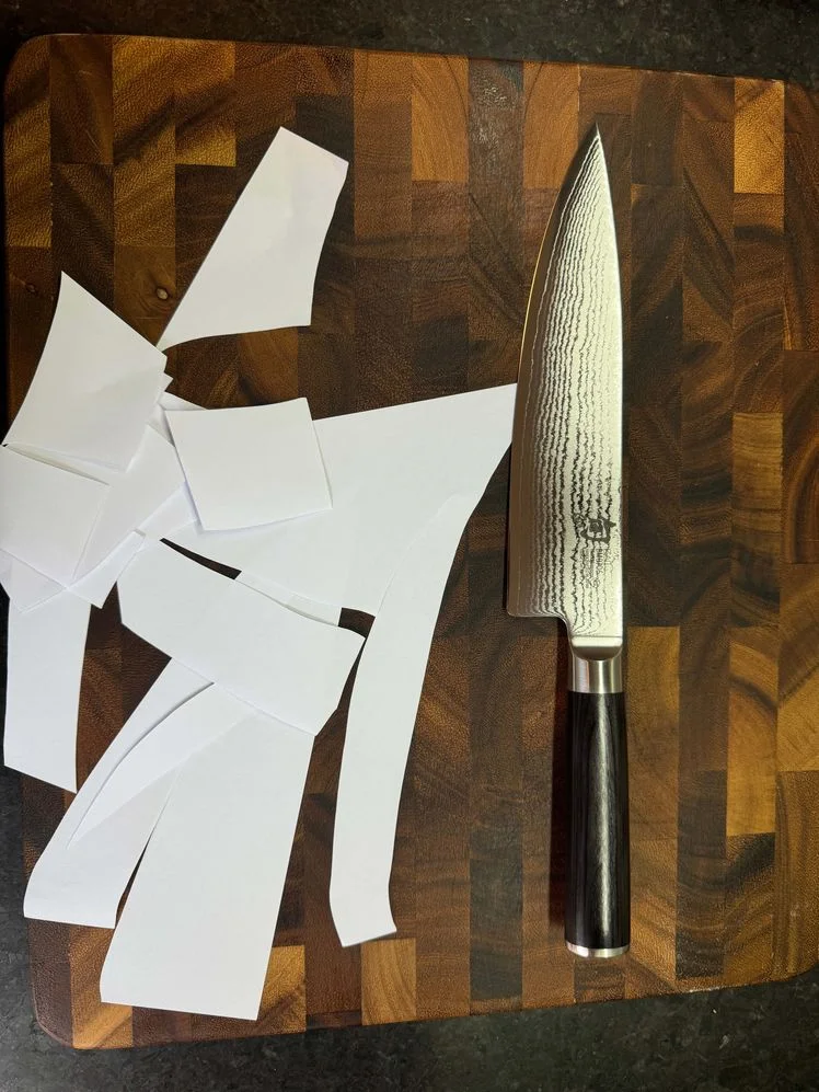 Shun Classic Chef's Knife sitting on a cutting board next to chopped up pieces of paper 