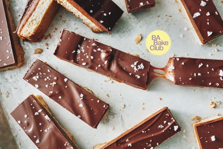 Bars of chocolate caramel and shortbread on a baking sheet topped with flakey salt.